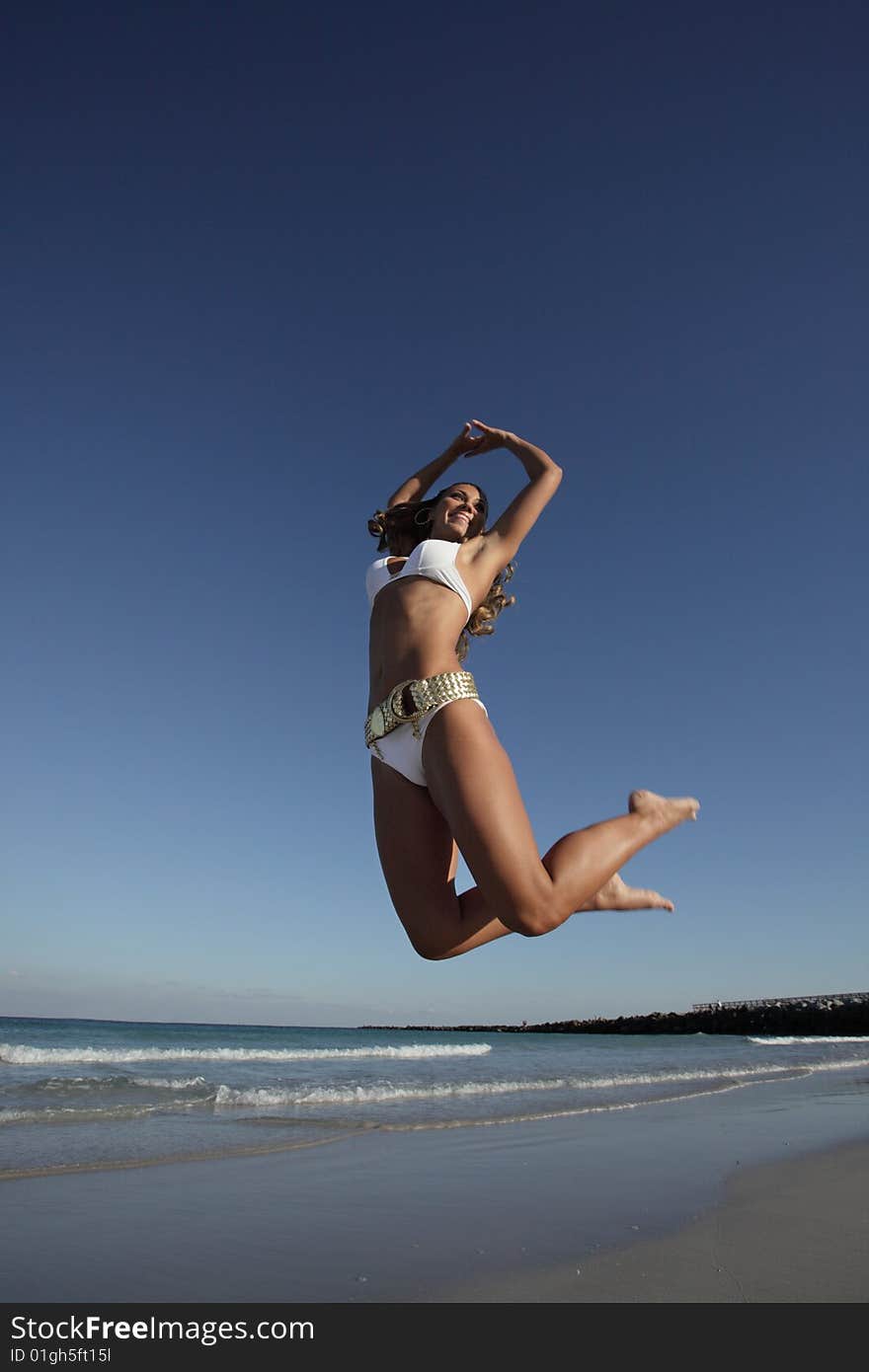 Young woman jumping on the beach on a deep blue sky. Young woman jumping on the beach on a deep blue sky