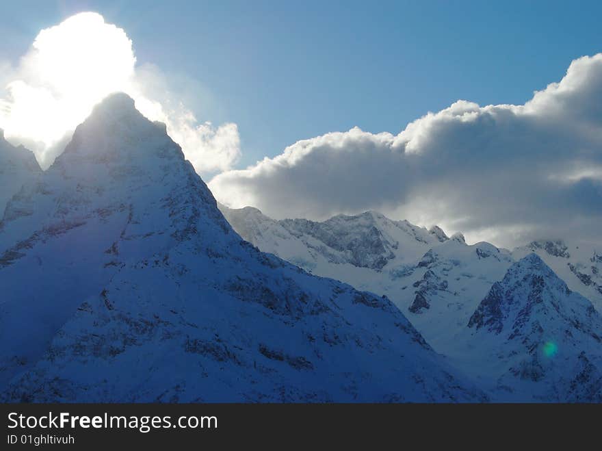 Snow covered steeply rocks and bright sky sunset