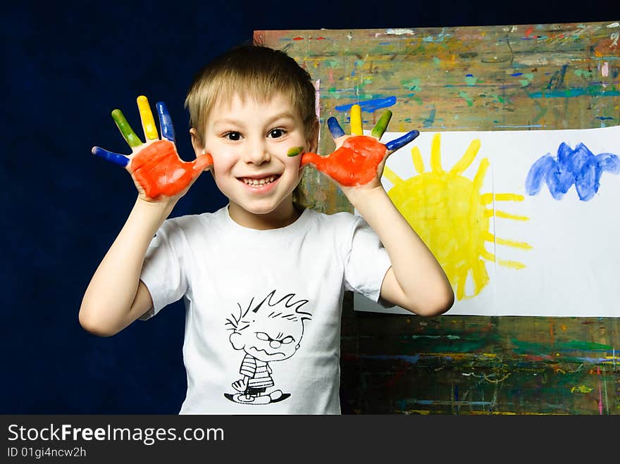 Cheerful little boy standing near the easel and showing his dirty fingers. Cheerful little boy standing near the easel and showing his dirty fingers