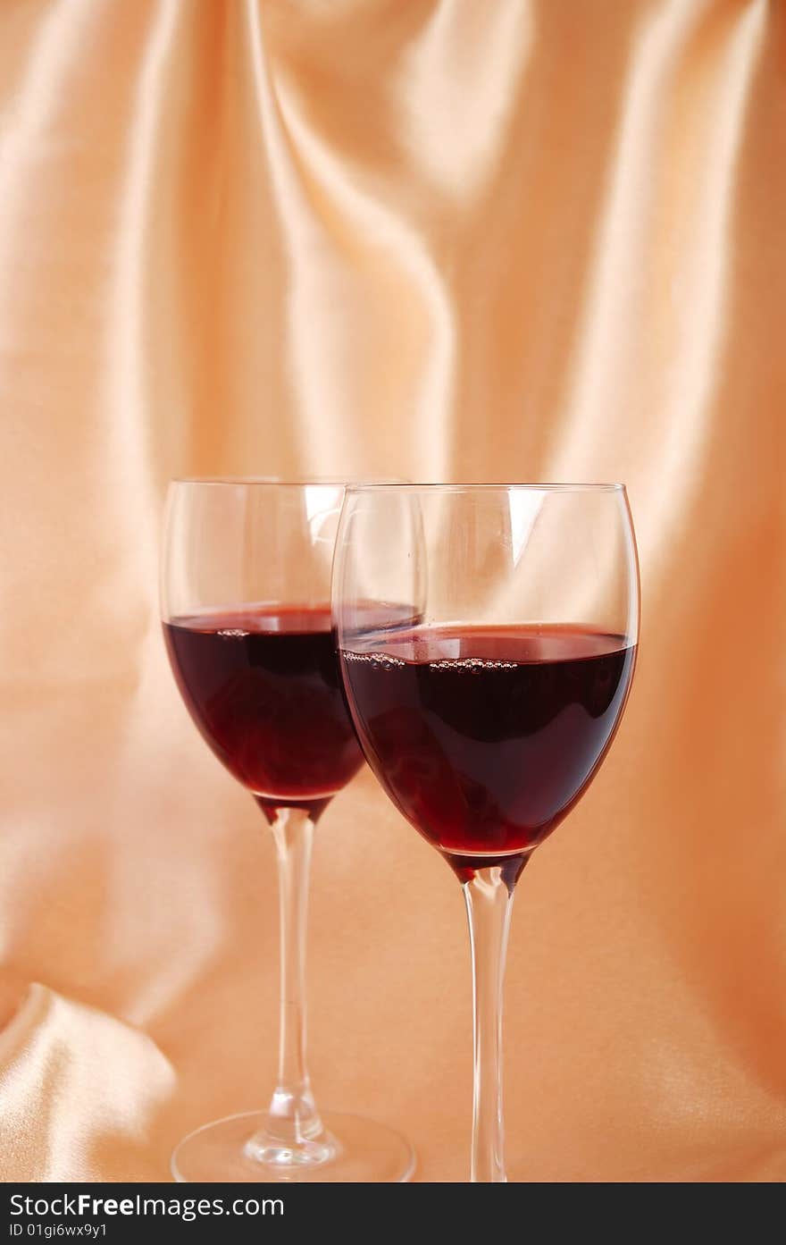 Two glasses with red wine on a beige satin background