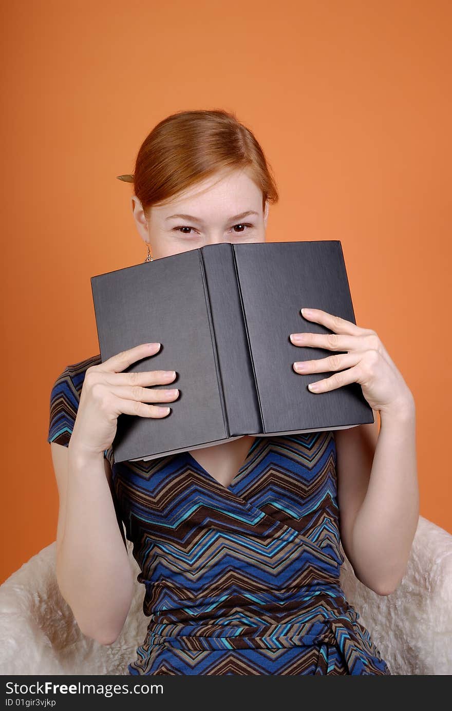 Young woman sits in an armchair and hides the face behind the book. Young woman sits in an armchair and hides the face behind the book