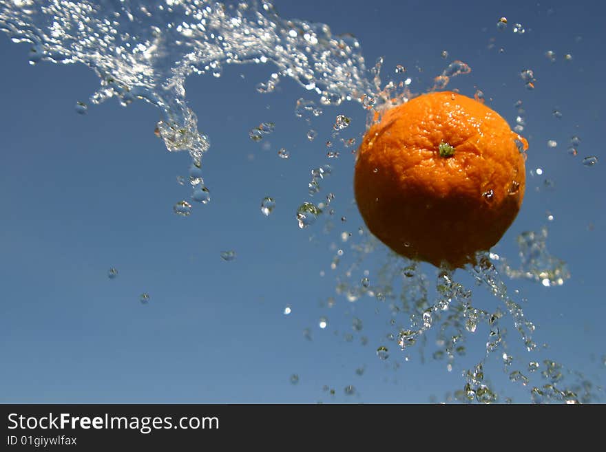 Orange flying through being sprayed by water on a blue sky background. Orange flying through being sprayed by water on a blue sky background.