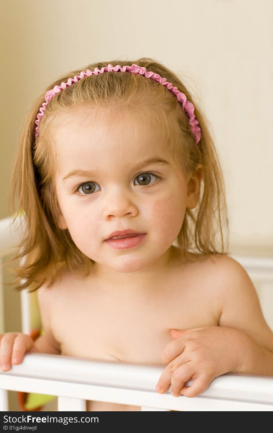 Beautiful baby girl standing up in her cot just before bedtime