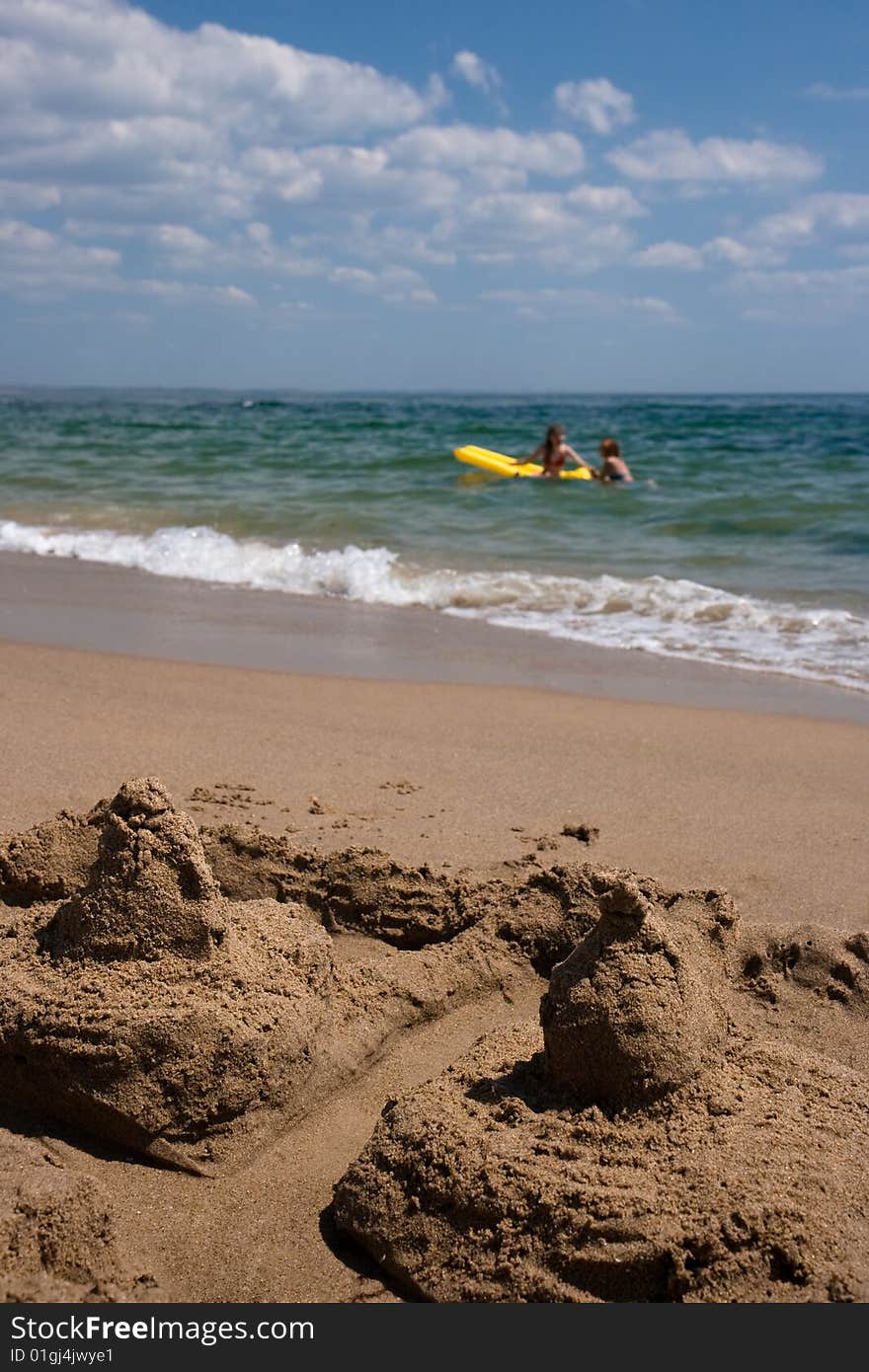 Sand castle and girls bathing in the sea