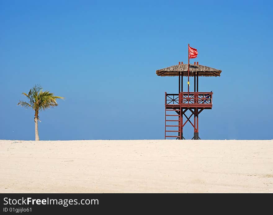 Red flag on the beach. A lifeguards hut ant palm tree. Red flag on the beach. A lifeguards hut ant palm tree.