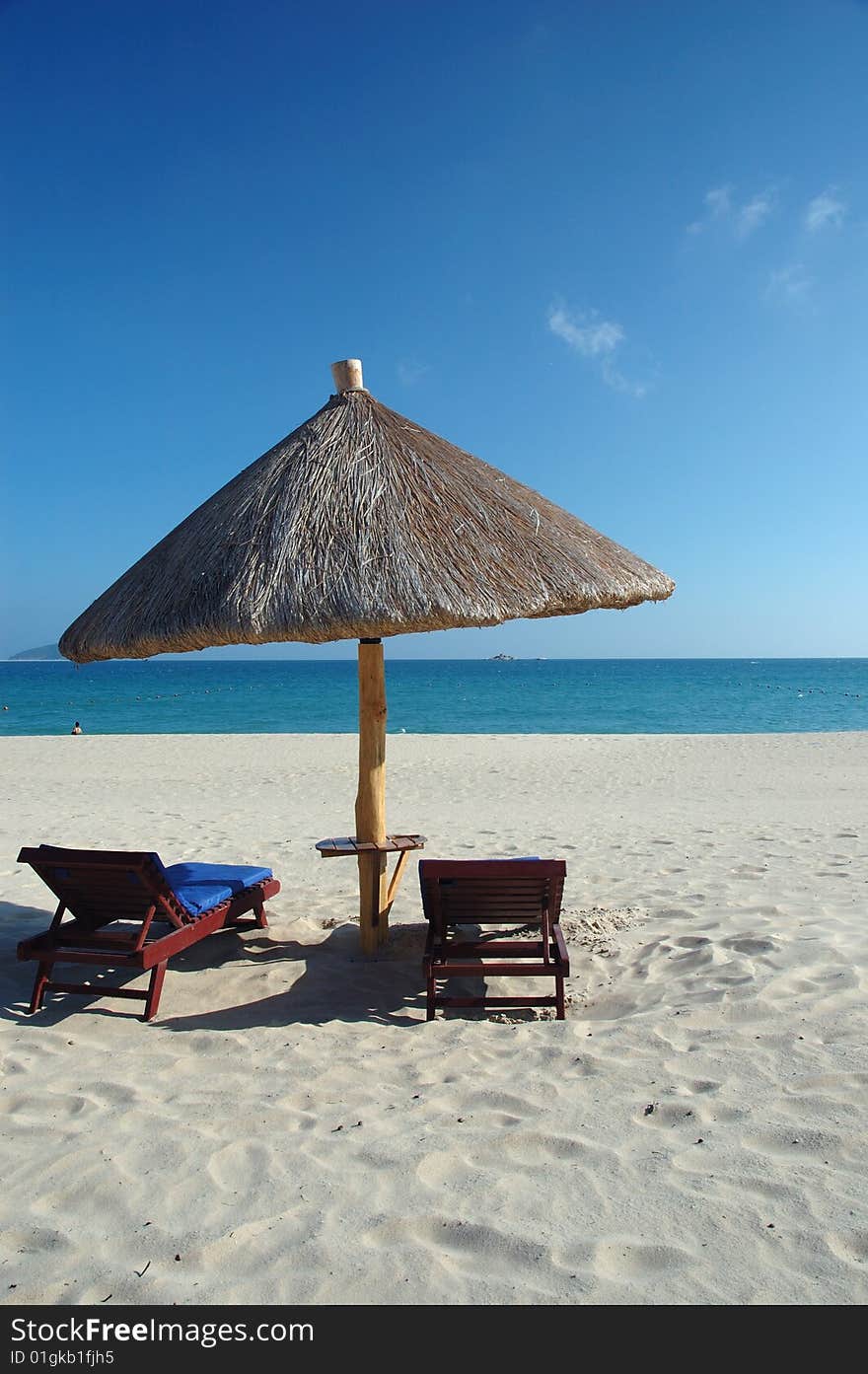 Two beach chairs under a parasol on the white sandy beach at a resort. Two beach chairs under a parasol on the white sandy beach at a resort.