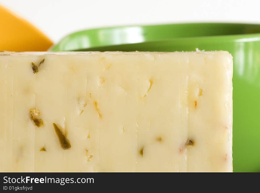 Macro cheese close-up of long rectangular shaped white orange wedge of aged monteray jack and jalepano pepper cheese containing showing the texture of the cheese sitting on black plate against a white wall with the crumbly texture of the aromatic cheese with green cup yellow cup