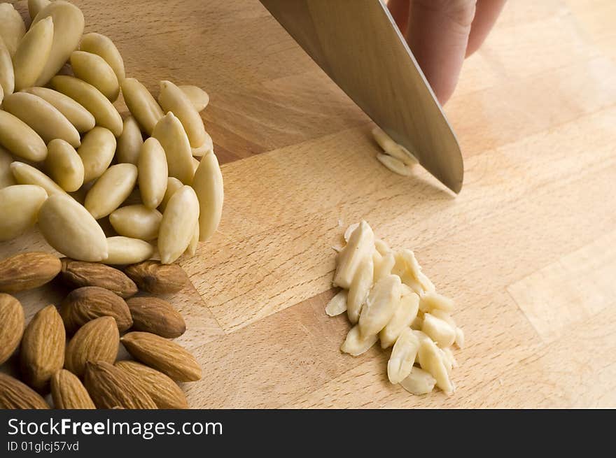 Hand chopping almond alongside pile of natural and peeled almonds on chopping board. Hand chopping almond alongside pile of natural and peeled almonds on chopping board.