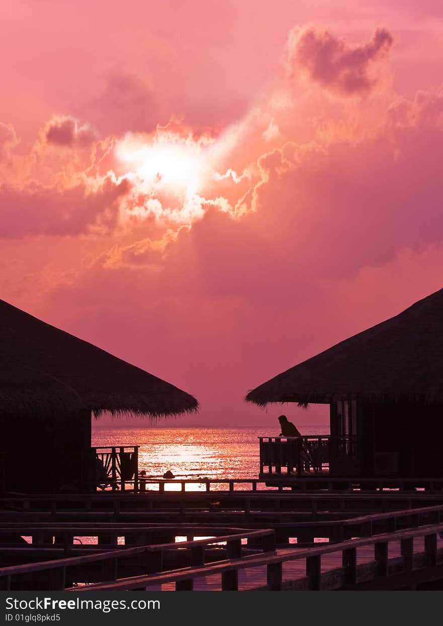 Human silhouette in water bungalow at sunset, abstract vacation background