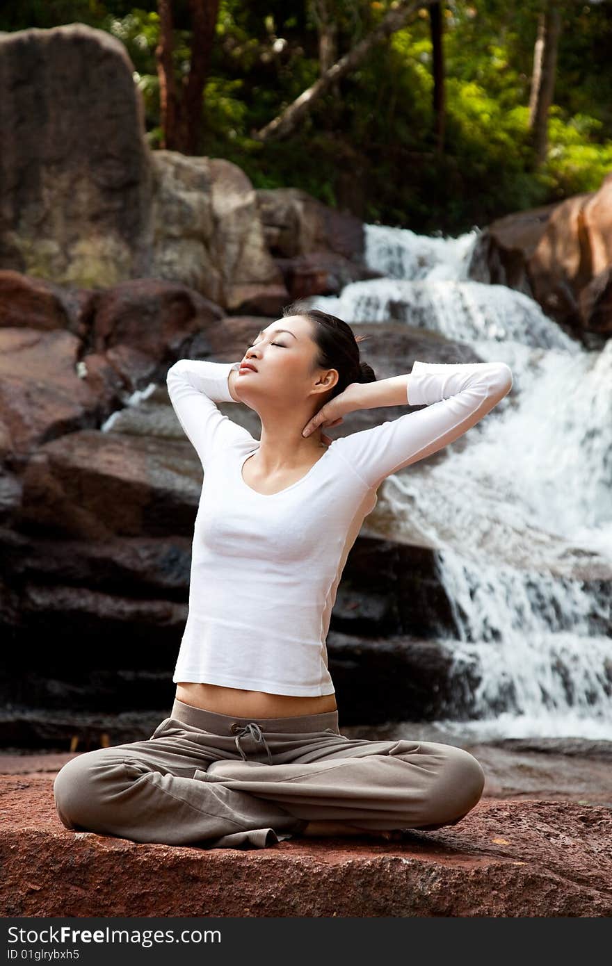 Outdoor young woman sitting by the waterfall meditating. Outdoor young woman sitting by the waterfall meditating