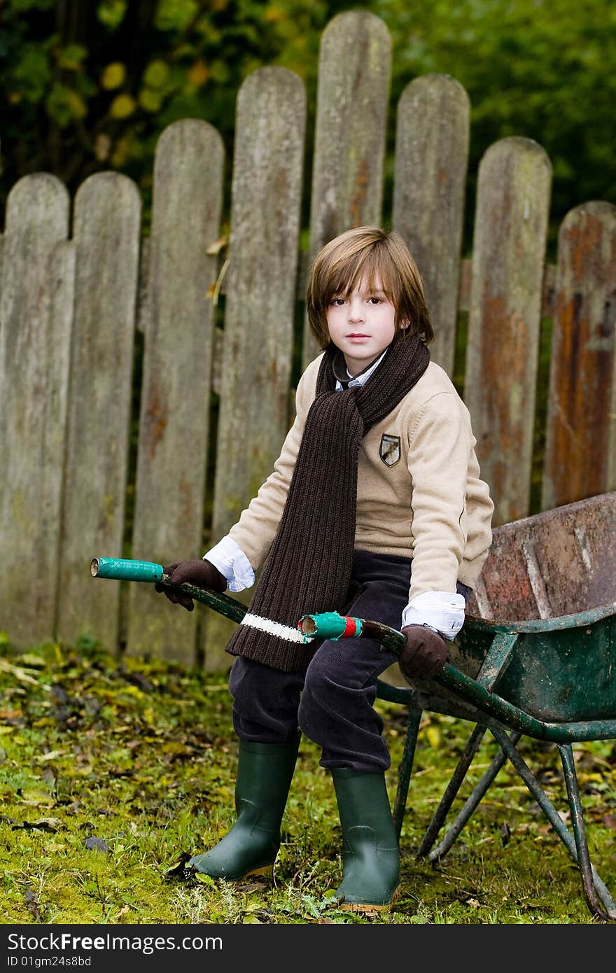 Closeup cute young boy sitting on a wheelbarrow in garden. Closeup cute young boy sitting on a wheelbarrow in garden