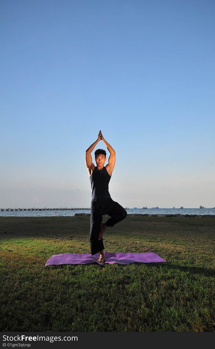 Picture of man doing yoga by the beach.