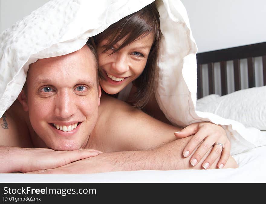 Young couple in their bed. They are playing in romance under the sheets. Young couple in their bed. They are playing in romance under the sheets.