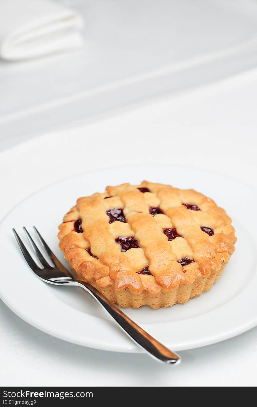 Small cherry pie on white saucer with fork