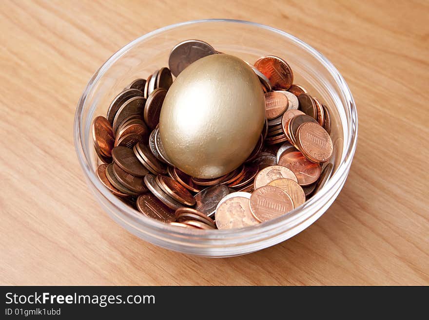 A golden egg laying in a bed of coins in a bowl as if a nest egg