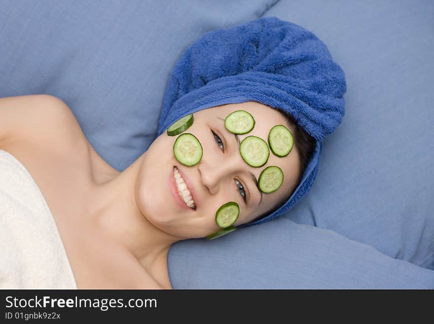 Portrait of smiling woman in dark blue towel and mask from cucumber. Portrait of smiling woman in dark blue towel and mask from cucumber