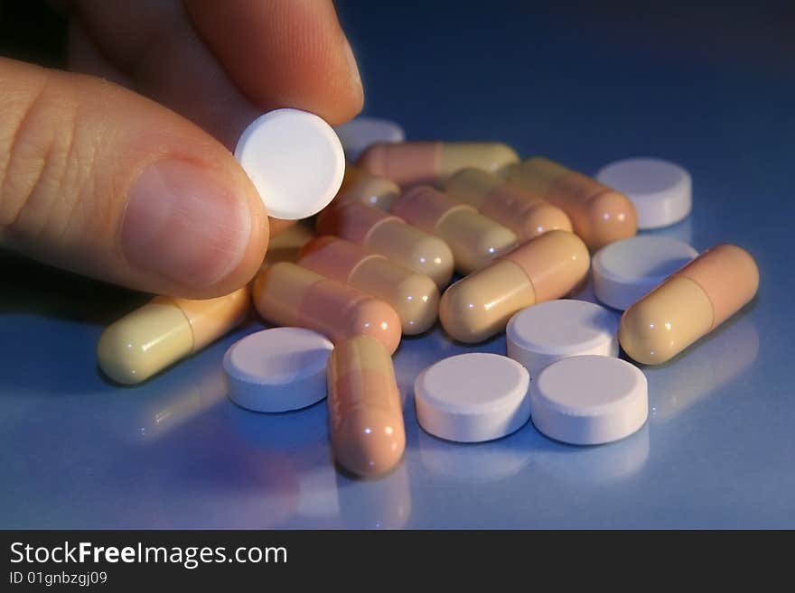 Round pills over blue background, one pill in fingers. Round pills over blue background, one pill in fingers