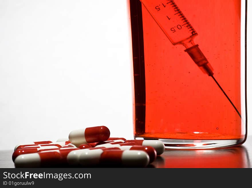 Tablets, a syringe into a glass with blood on a white background