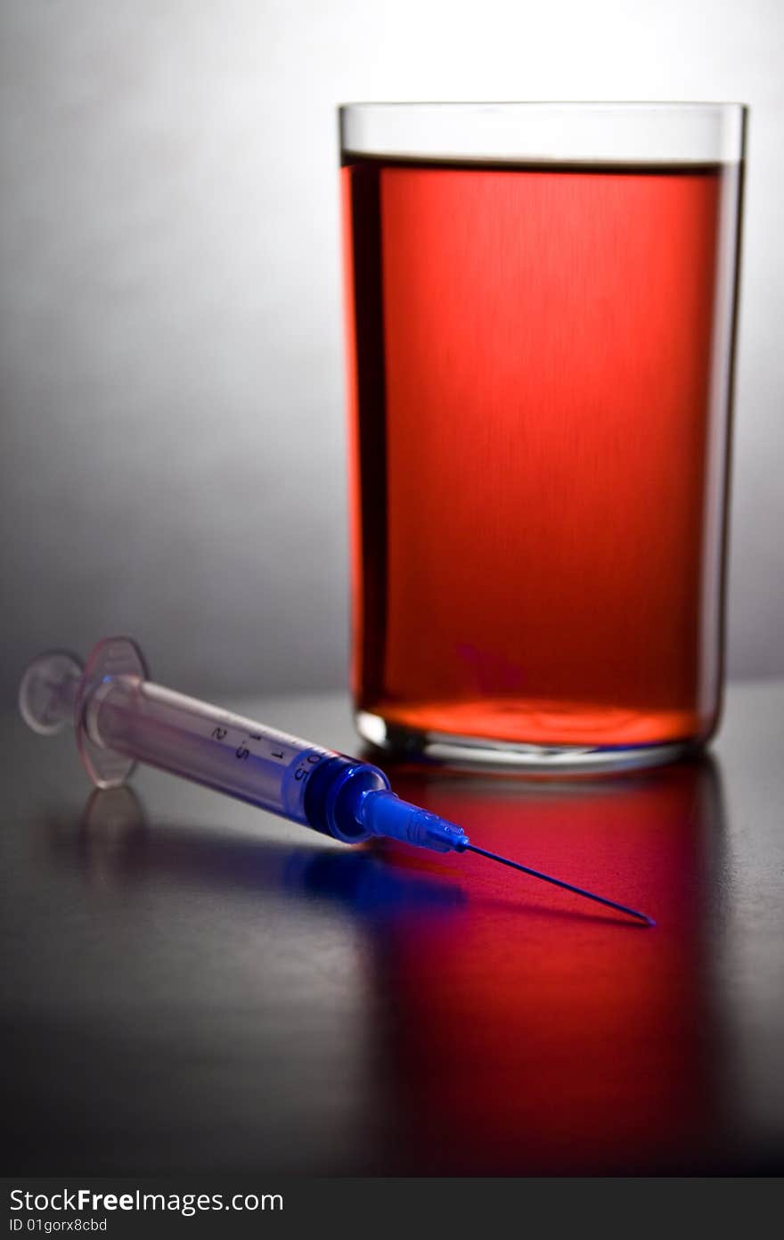 Syringe into a glass with blood  on a gray background