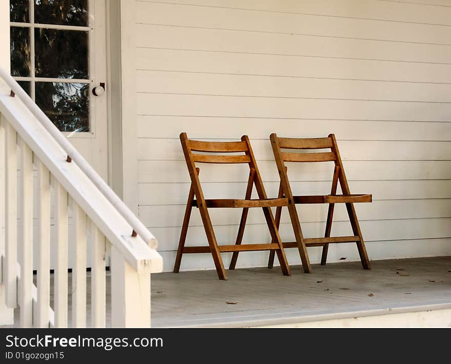 Two brown fold out chairs side by side on a porch. Two brown fold out chairs side by side on a porch.