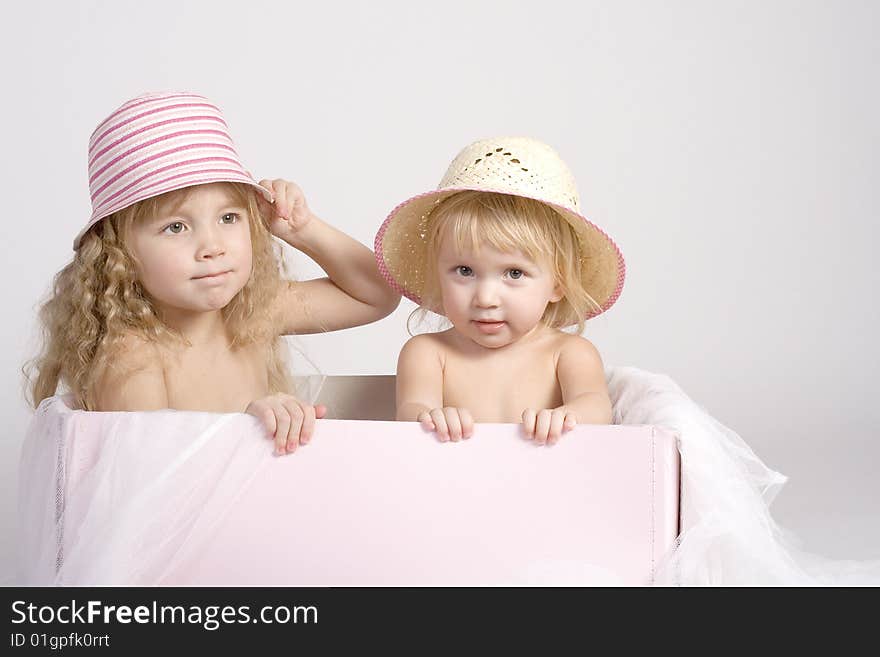 Two pretty sisters of 2 and 4 years old in summer bonnets sitting in big pink box