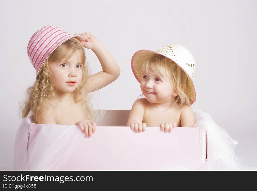 Two pretty sisters of 2 and 4 years old in summer bonnets sitting in big pink box