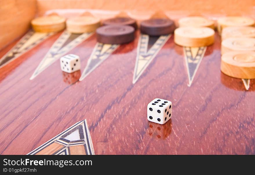 Closeup of one ivory dice and another in background on wooden handmade backgammon board with chips on white background. Closeup of one ivory dice and another in background on wooden handmade backgammon board with chips on white background