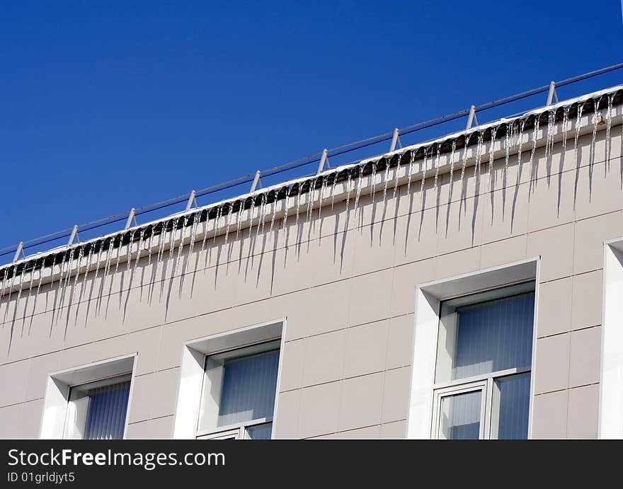 Long icicles winding from a roof buildings and blue sky. Long icicles winding from a roof buildings and blue sky