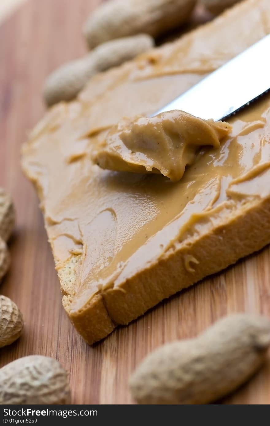 Slice of bread with peanut butter spread on wooden background.