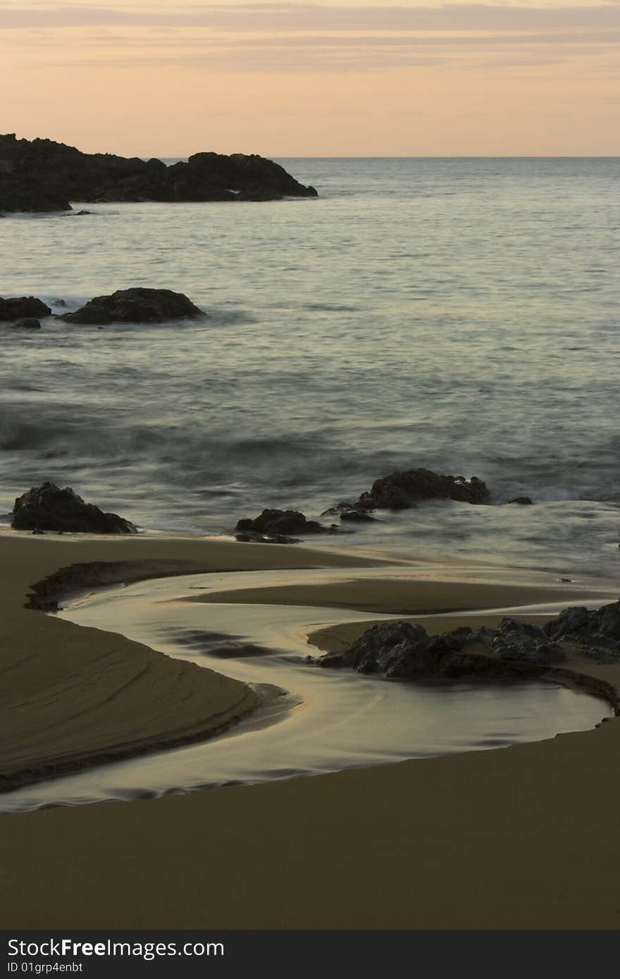 Water flows past rocks on a beach into the ocean at sunset. Water flows past rocks on a beach into the ocean at sunset