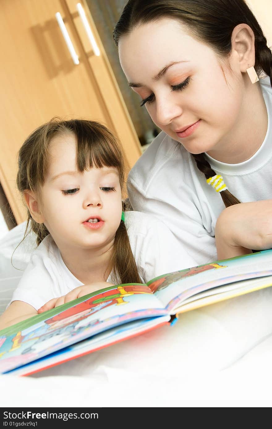 Young mother and her little daughter reading a book on the bed at home. Young mother and her little daughter reading a book on the bed at home