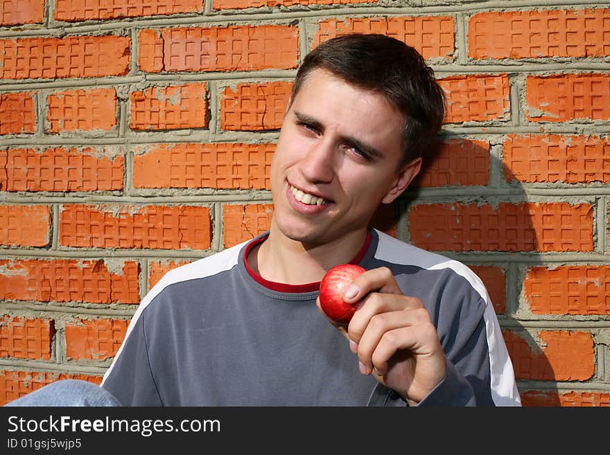 Young happy man with apple beside brick wall