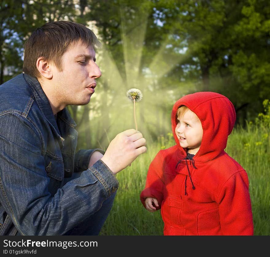 The daddy and a small daughter blow on a white dandelion