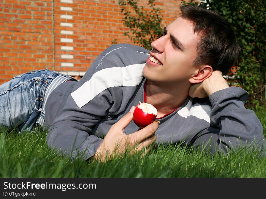 Young happy man with apple beside brick wall. Young happy man with apple beside brick wall