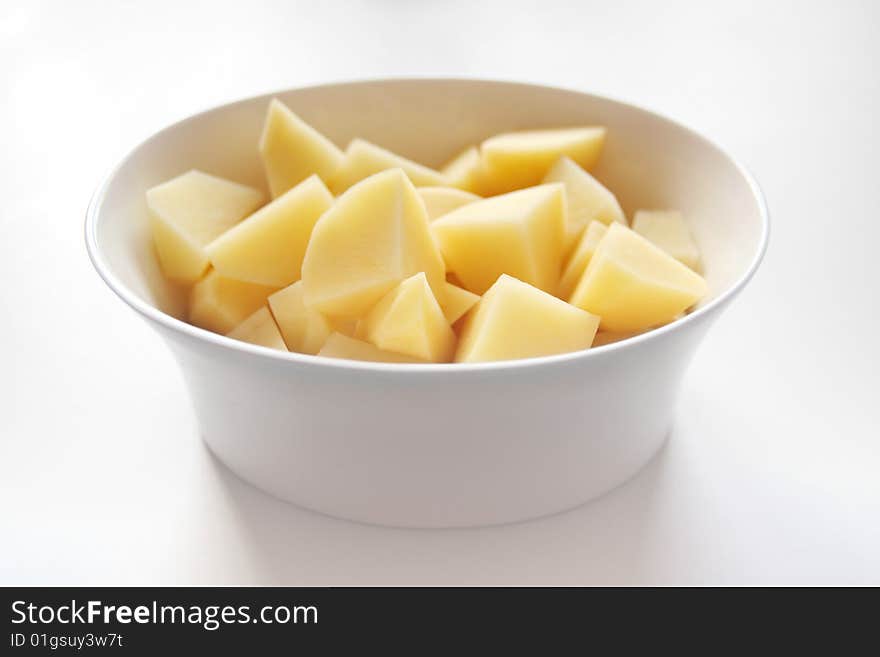 Peeled potatoe quarters in white dish at white table.