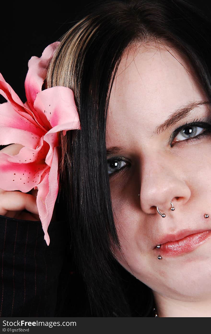 An pretty face shot with a pink flower and several piercing is looking in
the camera, on black background. An pretty face shot with a pink flower and several piercing is looking in
the camera, on black background.