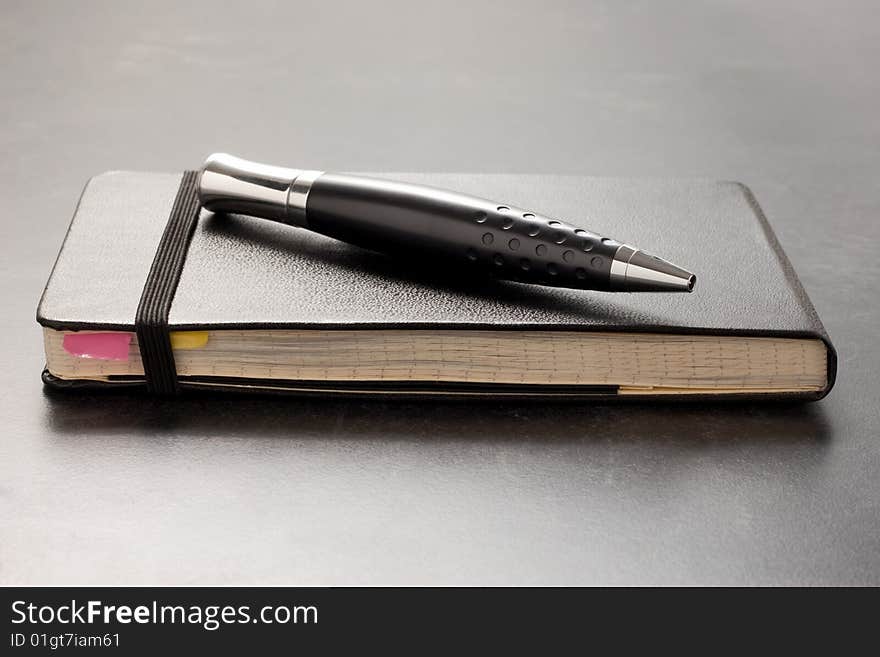 Black leather bound notebook on table with black shiny pen. Black leather bound notebook on table with black shiny pen.