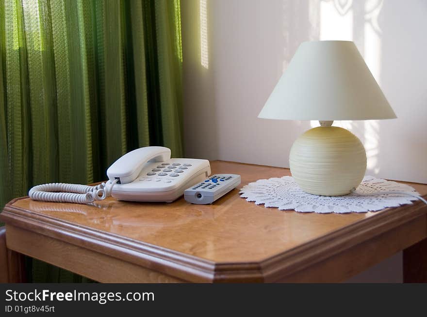 Corner of the room with phone, lamp and TV remote controller on table