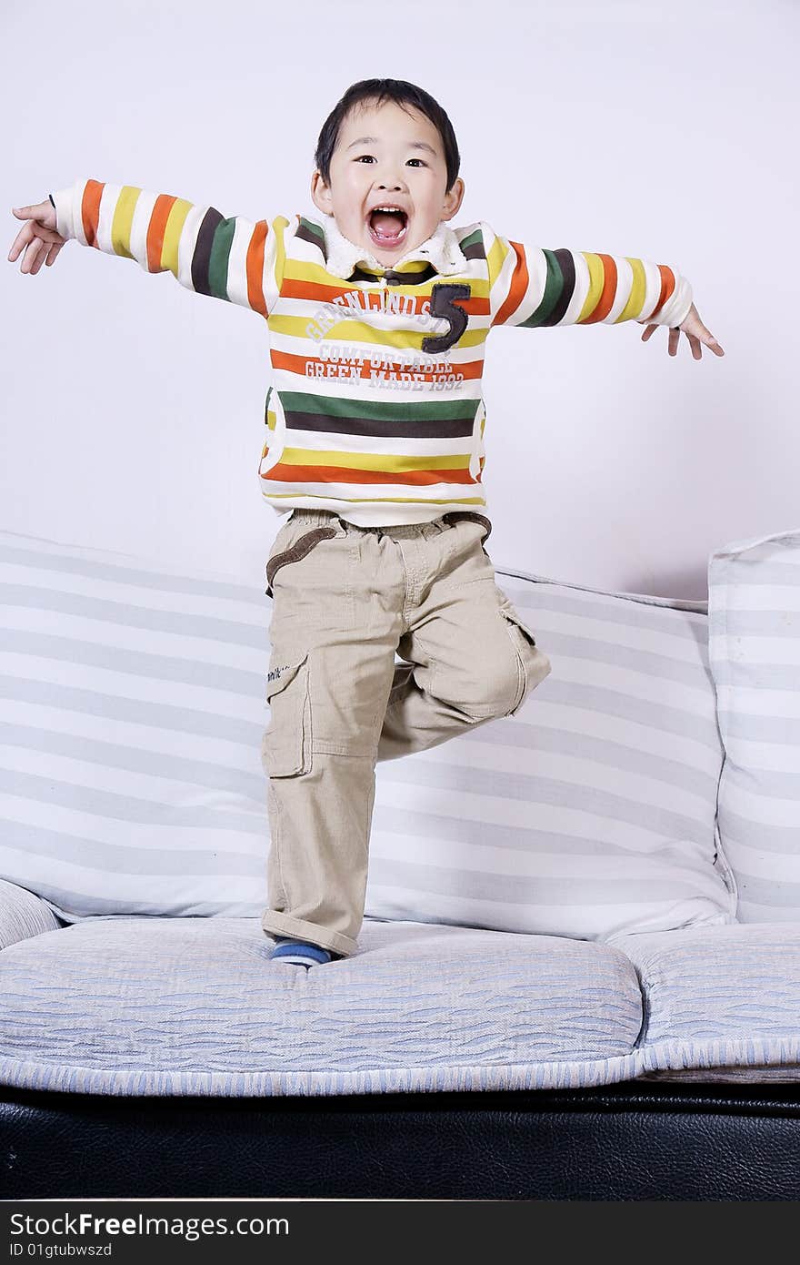 A picture of a little chinese boy playing roles and having great fun on sofa at home