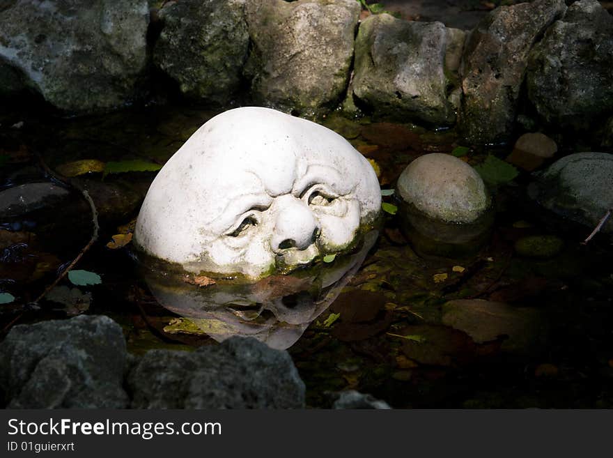 A sunlit decorative stone with carved face in a small pond. A sunlit decorative stone with carved face in a small pond