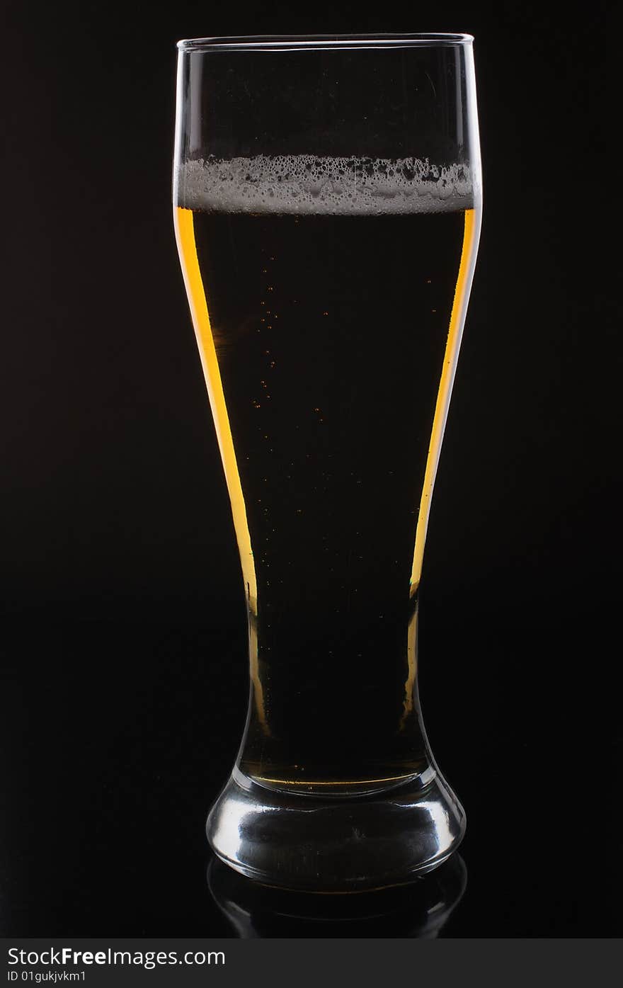 A glass of light beer on black background, lighted from behind. A glass of light beer on black background, lighted from behind