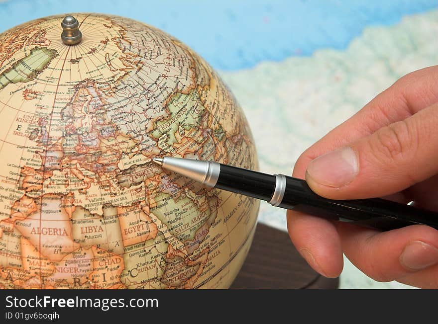 A hand holds the pen and indicates on the globe. A hand holds the pen and indicates on the globe