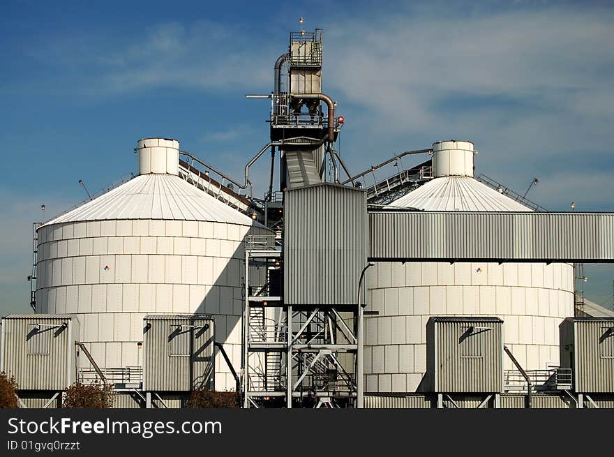 Two large tanks and conveyor belt at an oil refinery in an industrial neighborhood. Two large tanks and conveyor belt at an oil refinery in an industrial neighborhood.