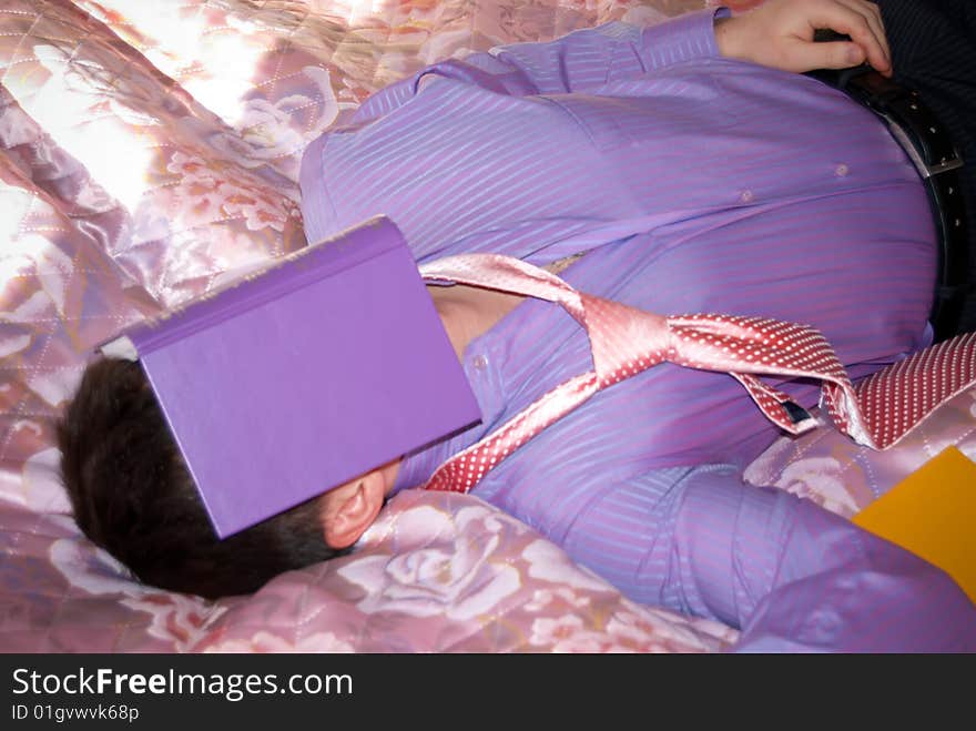 The young businessman who lays on a bed with the book on the face. The young businessman who lays on a bed with the book on the face.