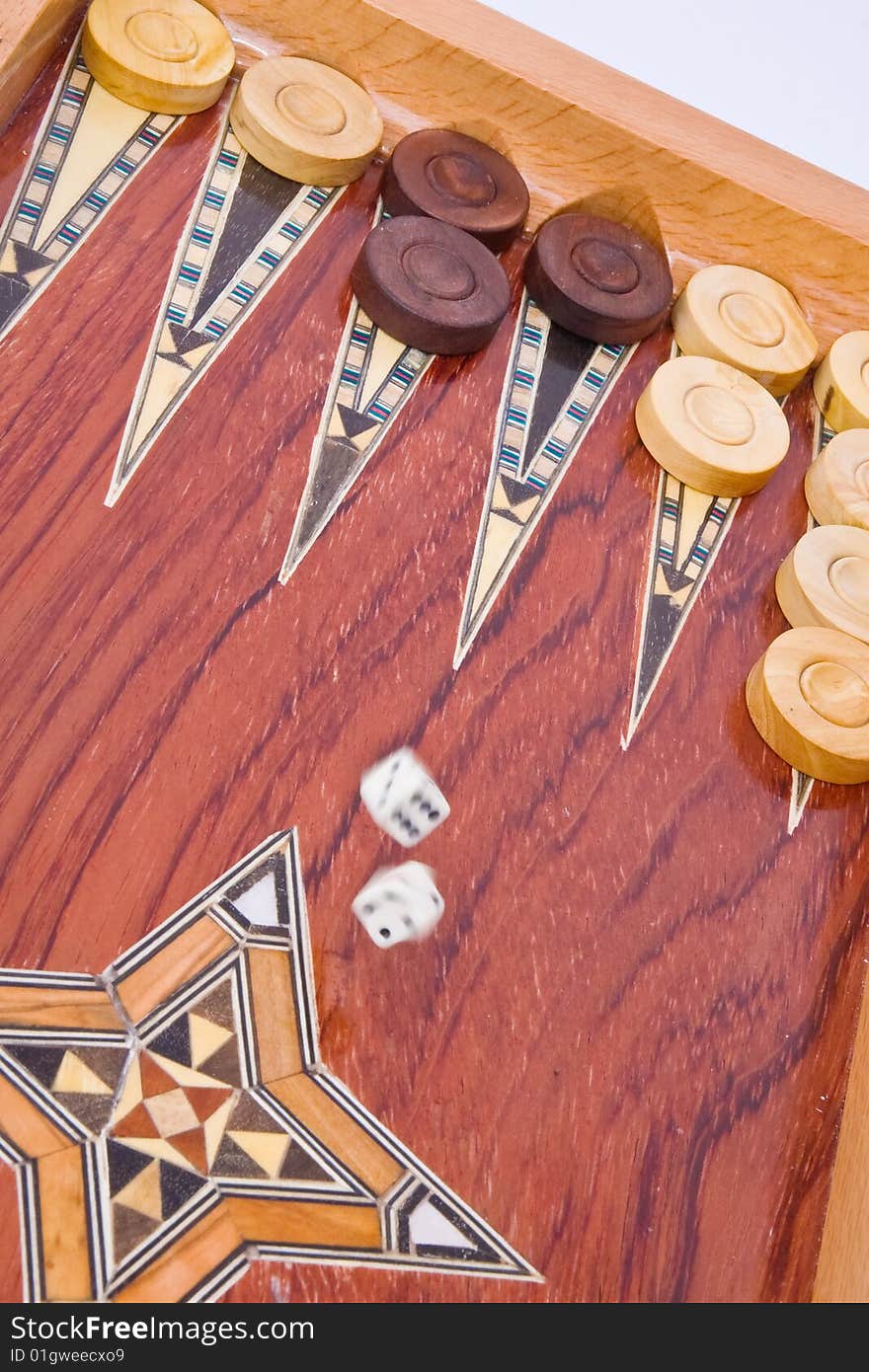 Two ivory dices falling on wooden handmade backgammon board with chips and on white background. Two ivory dices falling on wooden handmade backgammon board with chips and on white background