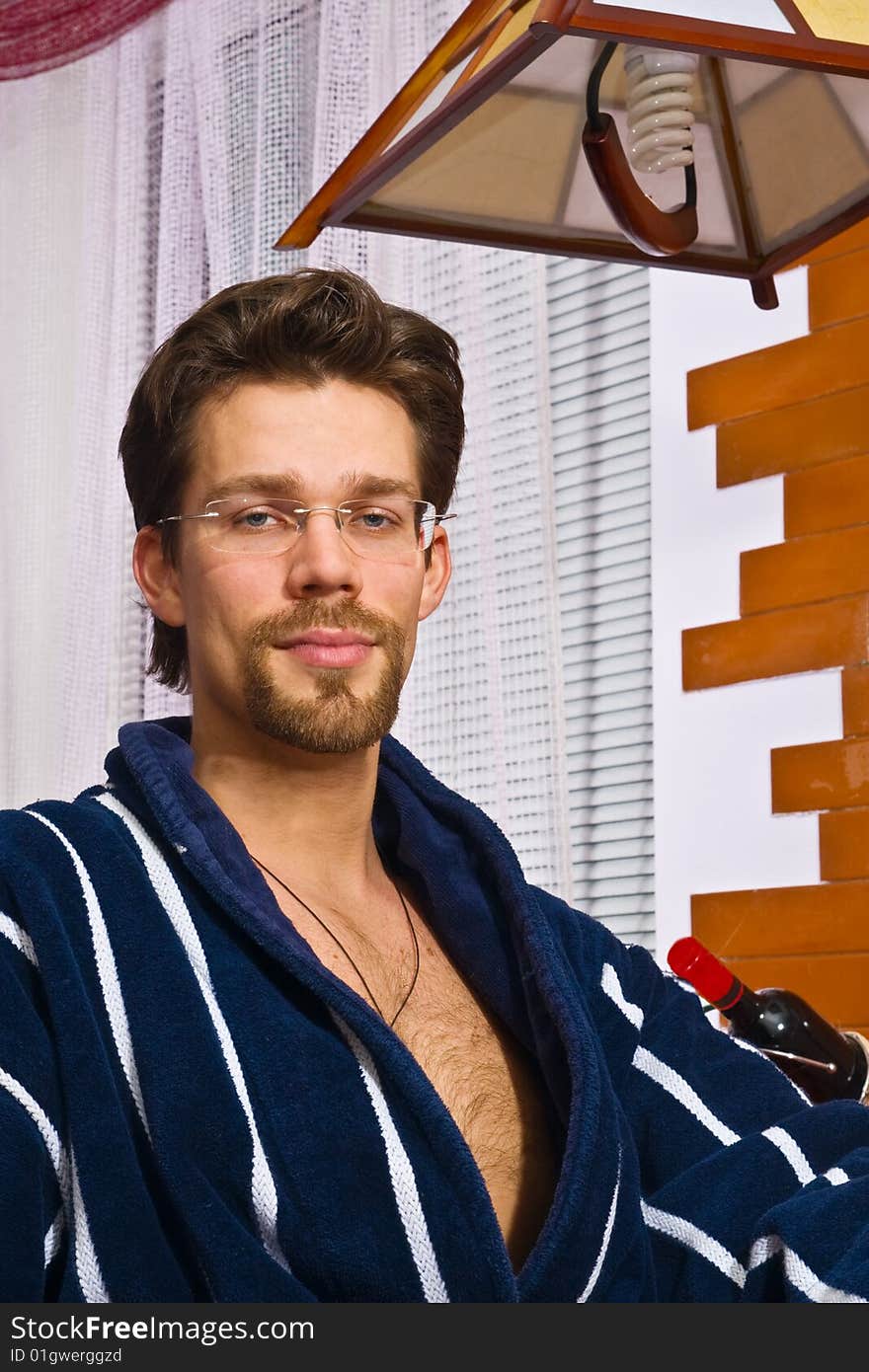 Young man wearing blue striped bathrobe sitting in his kitchen and smiling. Young man wearing blue striped bathrobe sitting in his kitchen and smiling