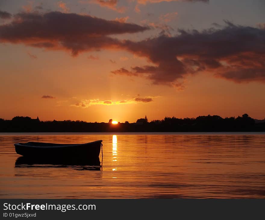 Dinghy silhouetted in sunrise over the bay.