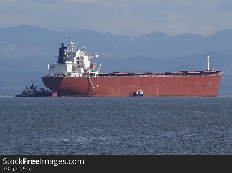 A cargo ship arrives with the assistance of tug boats. A cargo ship arrives with the assistance of tug boats.