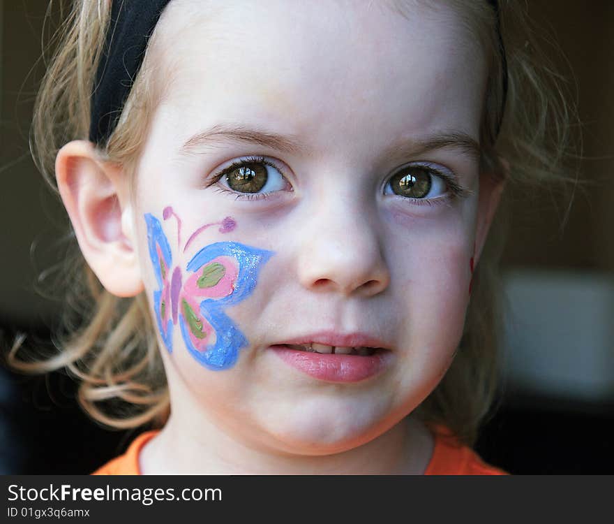 Little girl with beautiful brown eyes and a butterfly painted on her cheek. Little girl with beautiful brown eyes and a butterfly painted on her cheek.