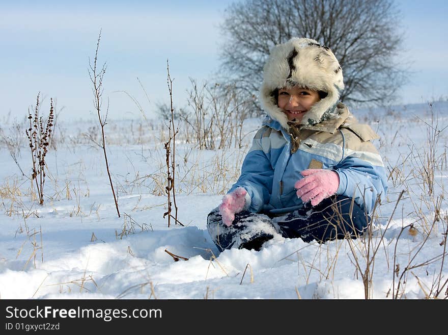 Cute girl in the fur-cap sitting in snow